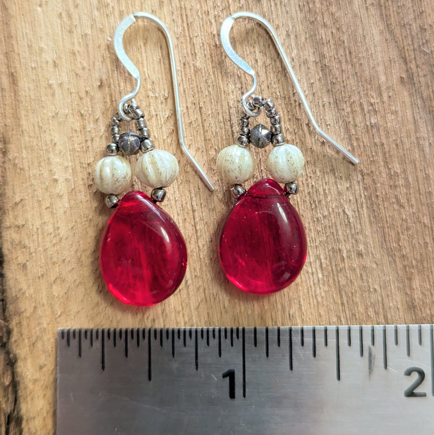 Red teardrop earrings with white beads on silver hooks, shown next to a ruler for size reference.