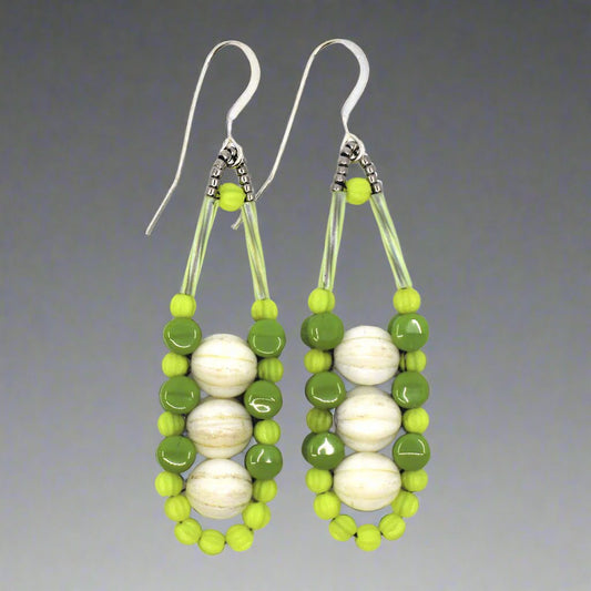 Cream and green earrings with silver accents and ear wires on a gray background. These earrings have three cream rounds stacked vertically like peas and held in place by an outline of bright chartreuse and darker avocado green beads.