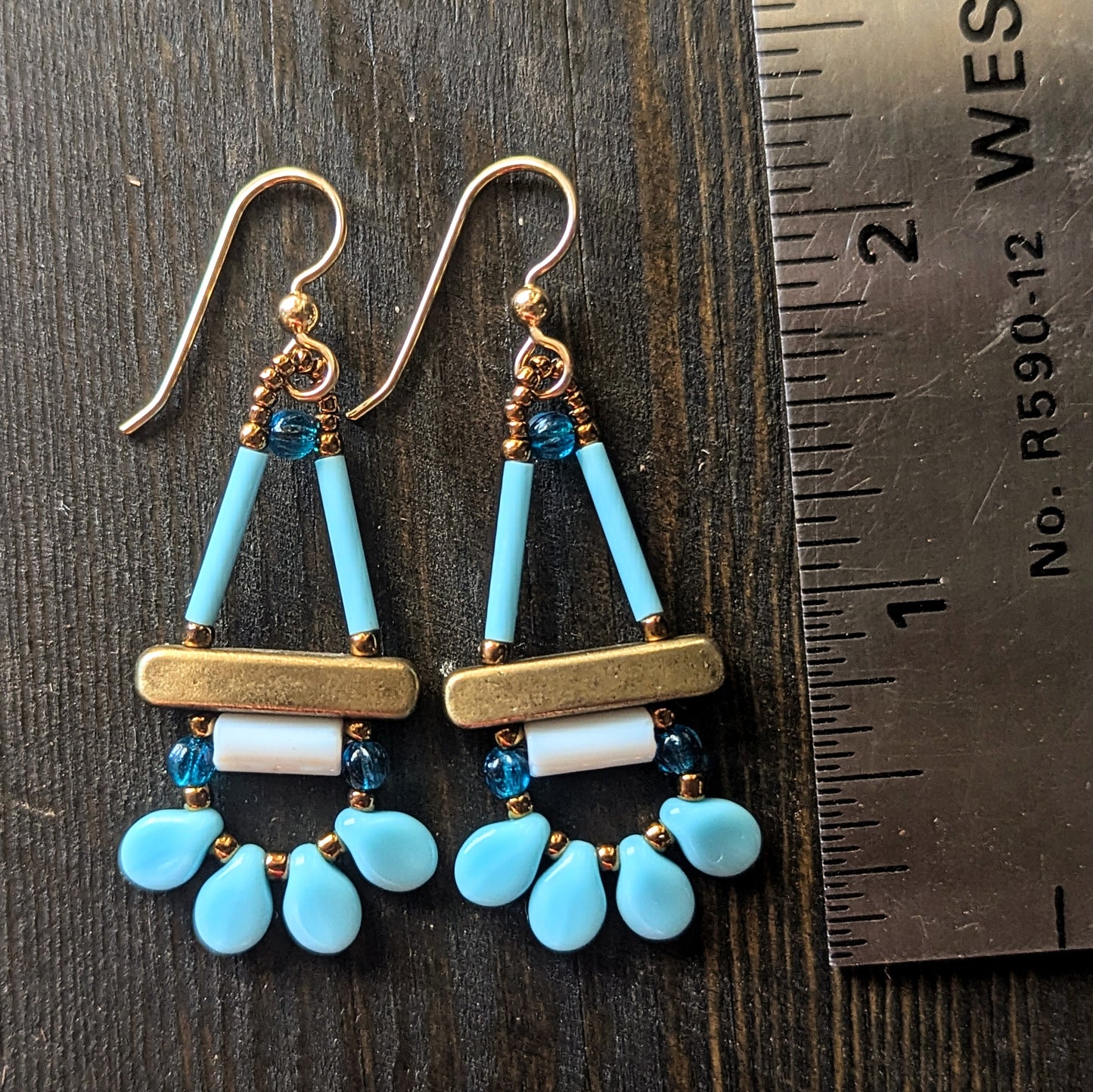 Pair of blue, white and gold earrings on a wooden surface with a ruler for scale.