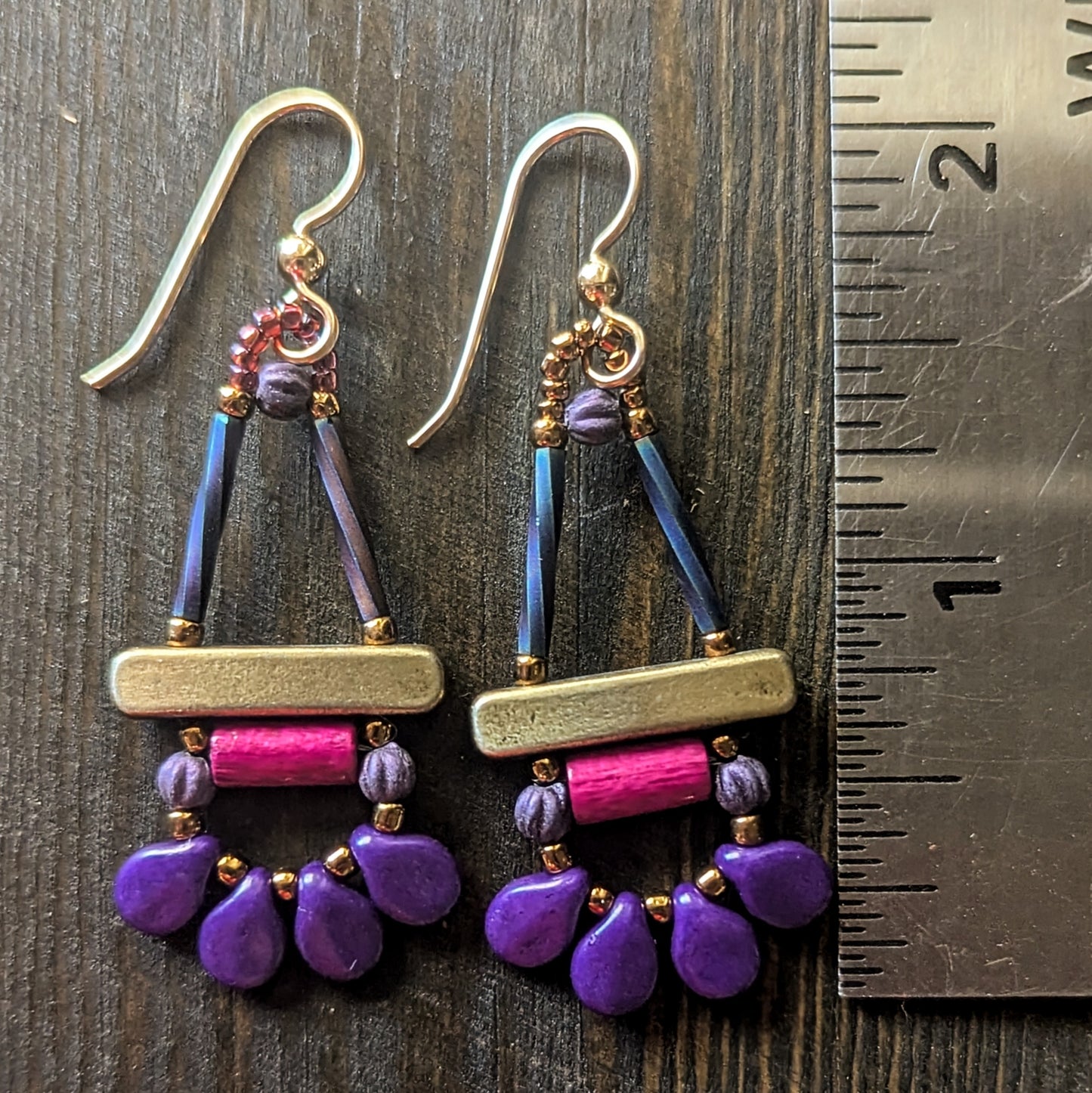 Colorful beaded earrings with purple and pink components, shown with a ruler for scale on a wooden surface