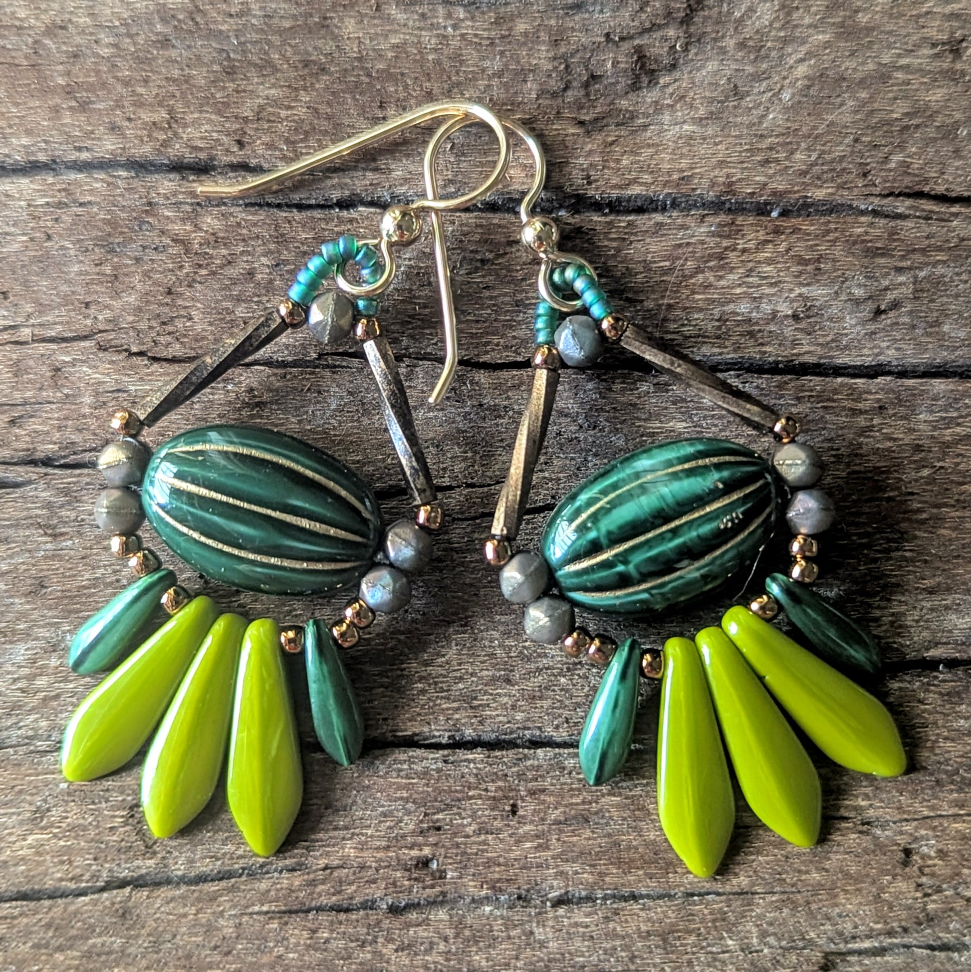 Pair of earrings with green and lime green beads on a wooden surface