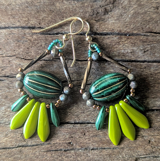 Pair of earrings with green and lime green beads on a wooden surface
