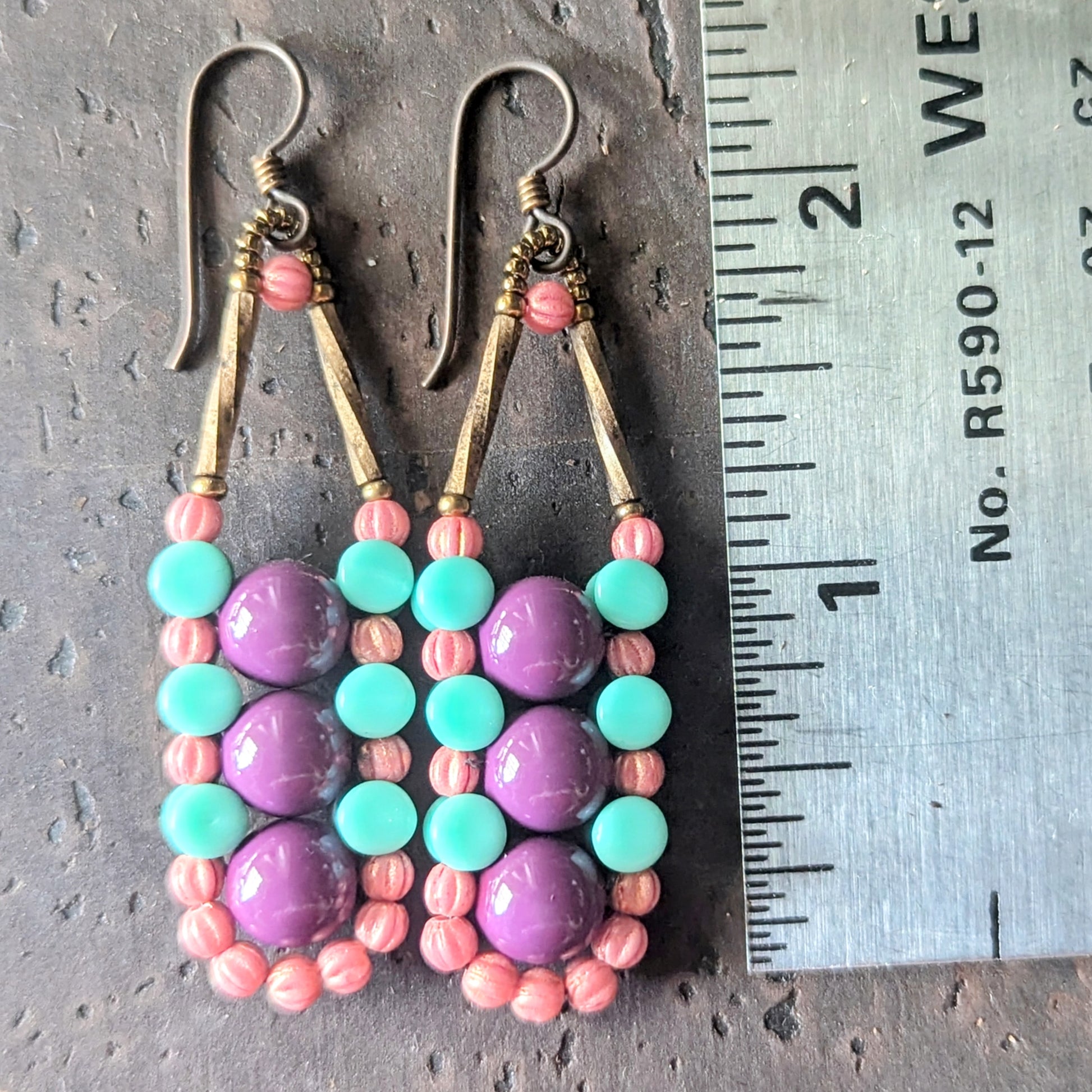 Beaded earrings with purple and turquoise beads on a metal surface with a ruler for scale.