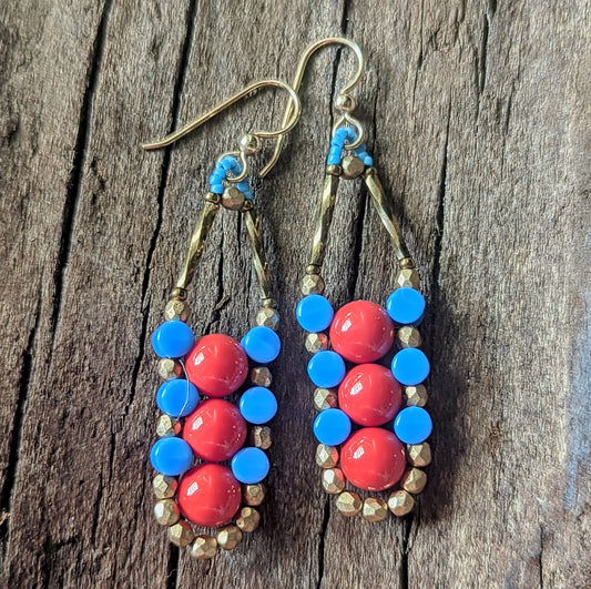 A pair of columnar earrings with red and blue beads on a wooden surface