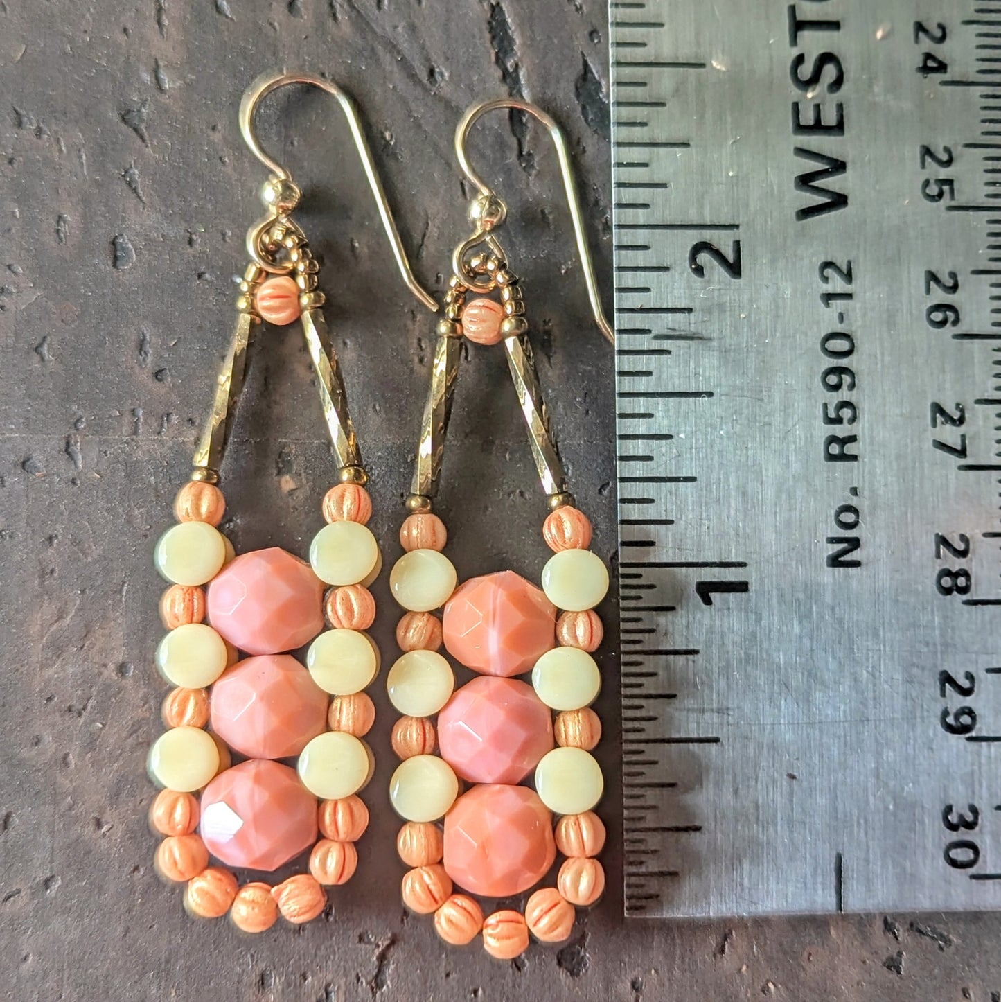Columnar beaded earrings with pink, cream and peach beads shown next to a ruler on a wooden surface.