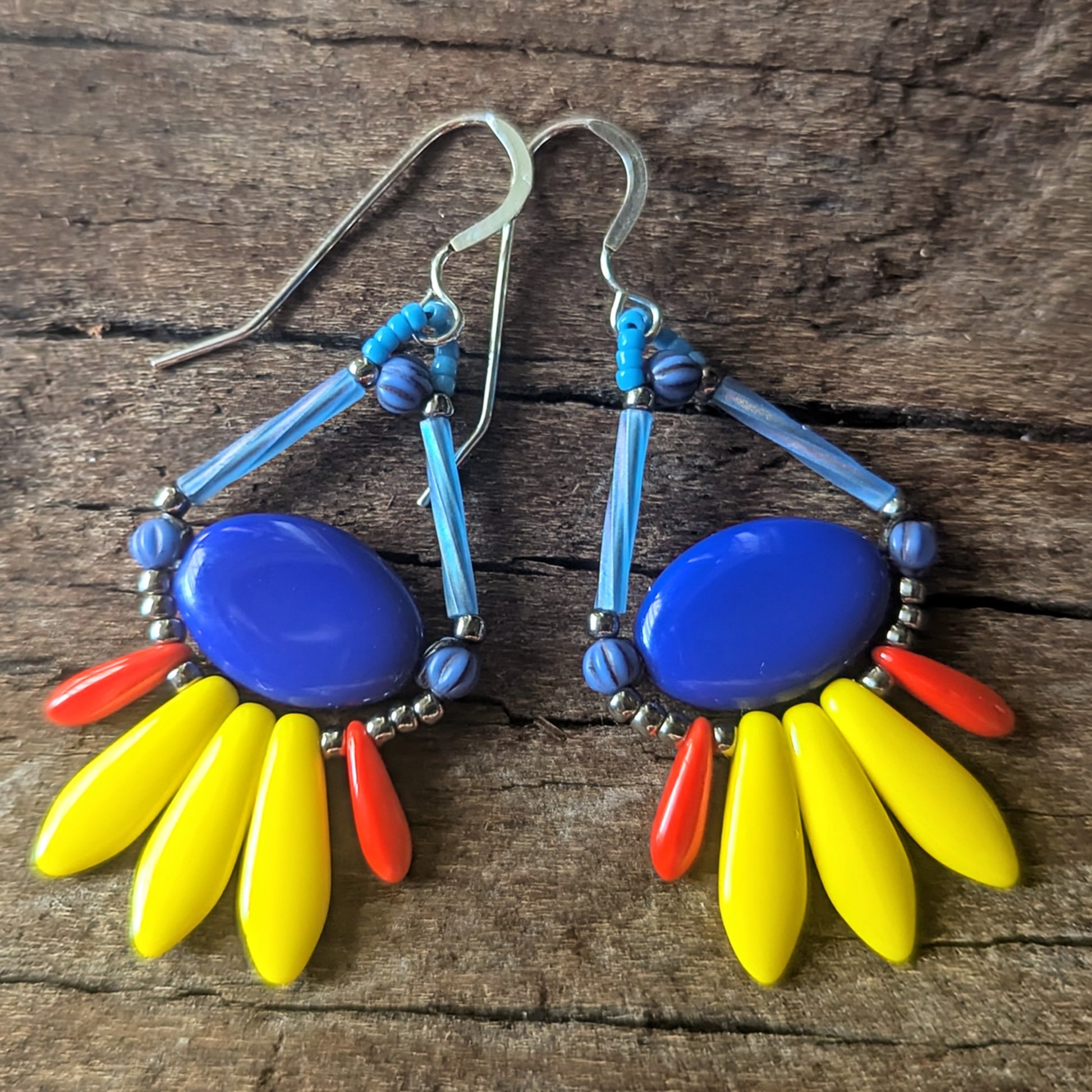 Colorful beaded earrings with blue, yellow, and red stones on a wooden surface
