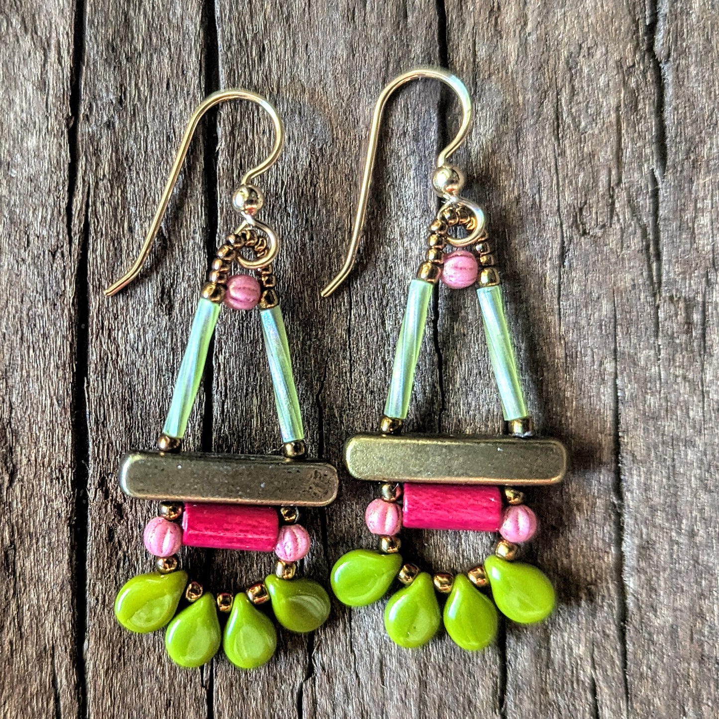 Colorful beaded earrings with gold, pink and green components on a wooden surface