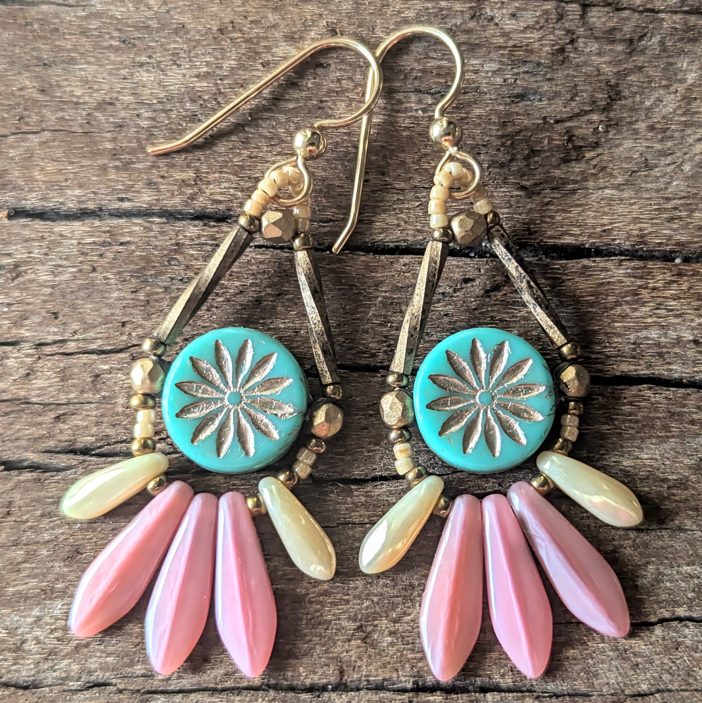 Earrings with turquoise center, gold accents, and pink and green fringe on a wooden surface