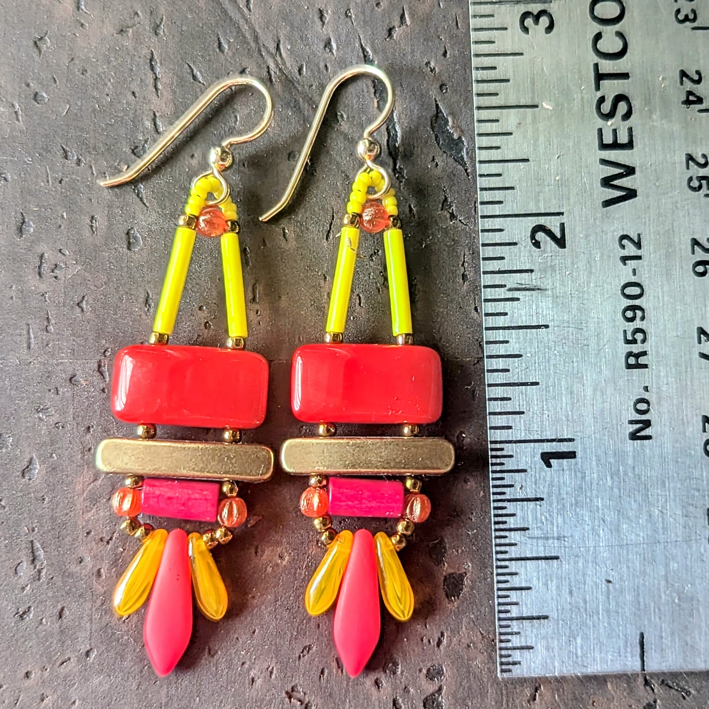 Colorful beaded earrings with red, pink, orange and yellow components on a wooden surface with a ruler for scale
