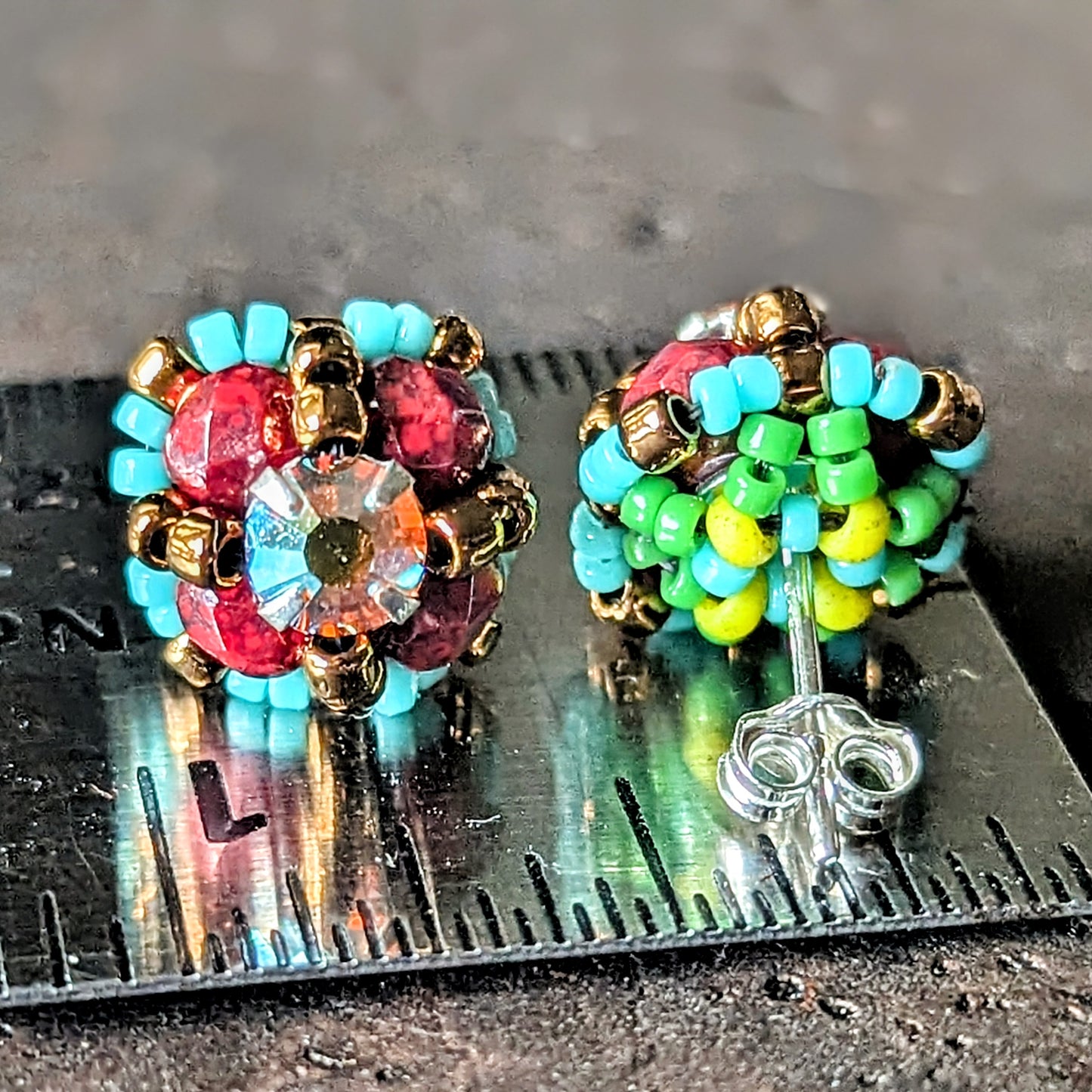A pair of burgundy and turquoise stud earrings shown front and back on a ruler for scale.