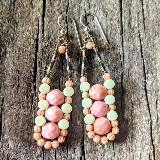 Columnar beaded earrings with pink, cream and peach beads on a wooden surface.