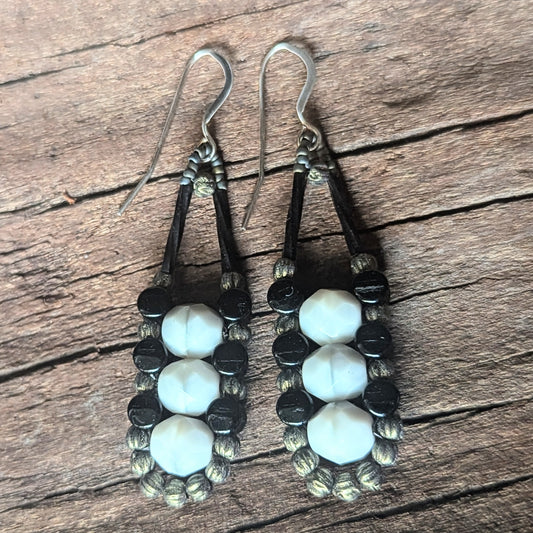 A columnar pair of gray and black beaded earrings on a wooden surface