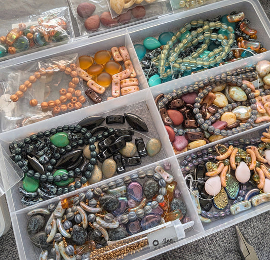 A divided plastic container with groupings of various colors and shapes of glass beads.