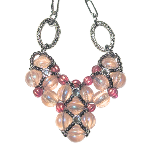 A pink beaded heart pendant with silver chain on a white background. The heart is made from pale pink melon beads with darker pink accents on the edges. The pink beadwork has an overlay of silver seed bead X-shapes with clear rhinestones in their centers. 
