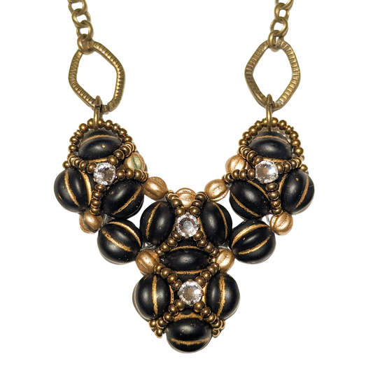 Heart shaped pendant on brass chain. The heart is made from gold-striped black beans overlaid with X-patterns of gold seed beads with clear rhinestones in the center.