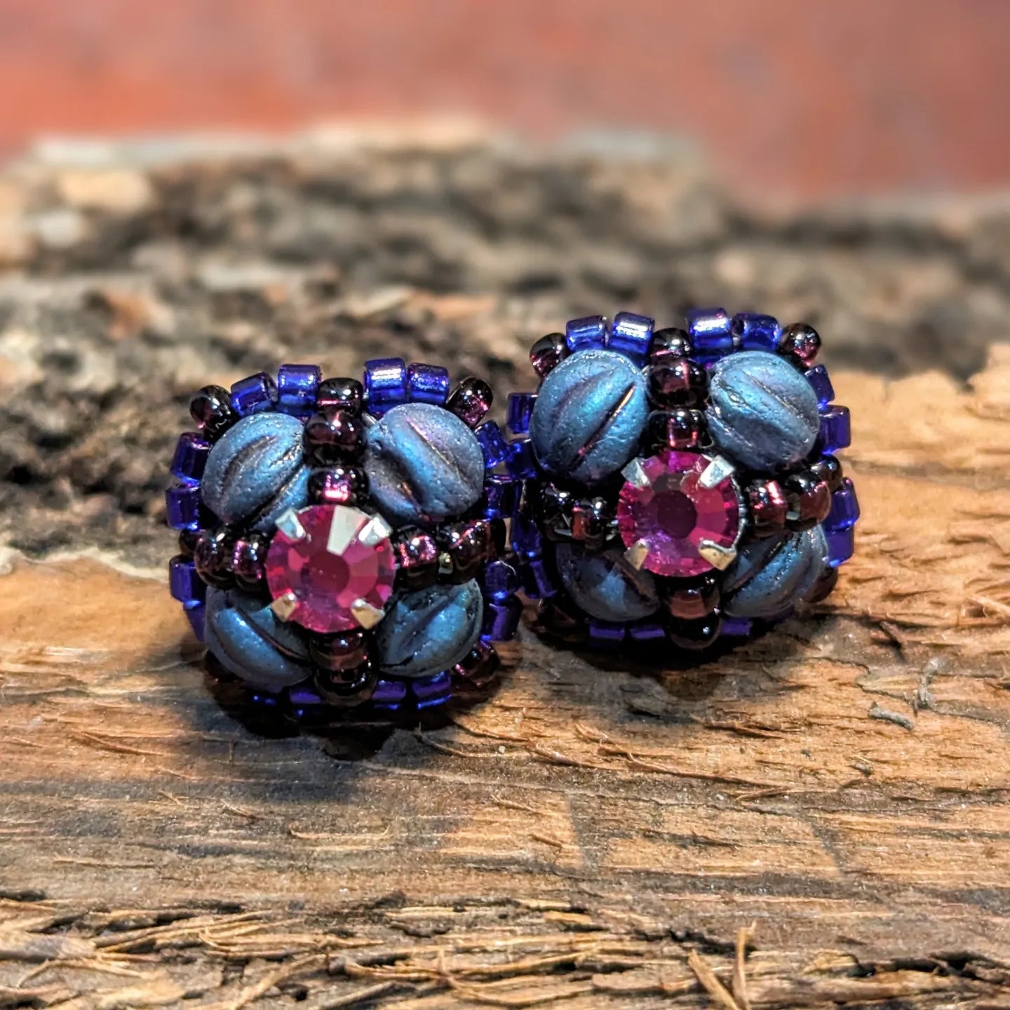 Four-sided purple and pink flower shaped stud earrings set on wood.