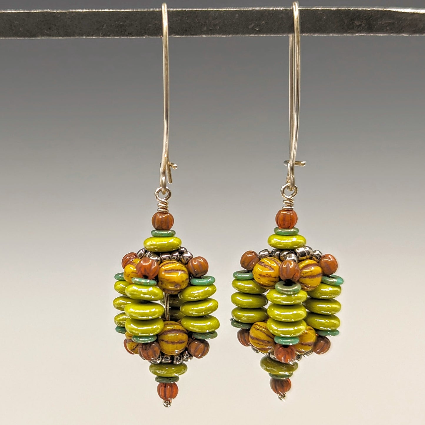 Beaded ball earrings on long silver ear wires. The beaded balls have four sides that are stacked chartreuse discs and the tops of the balls are mustard and rust colored beads.