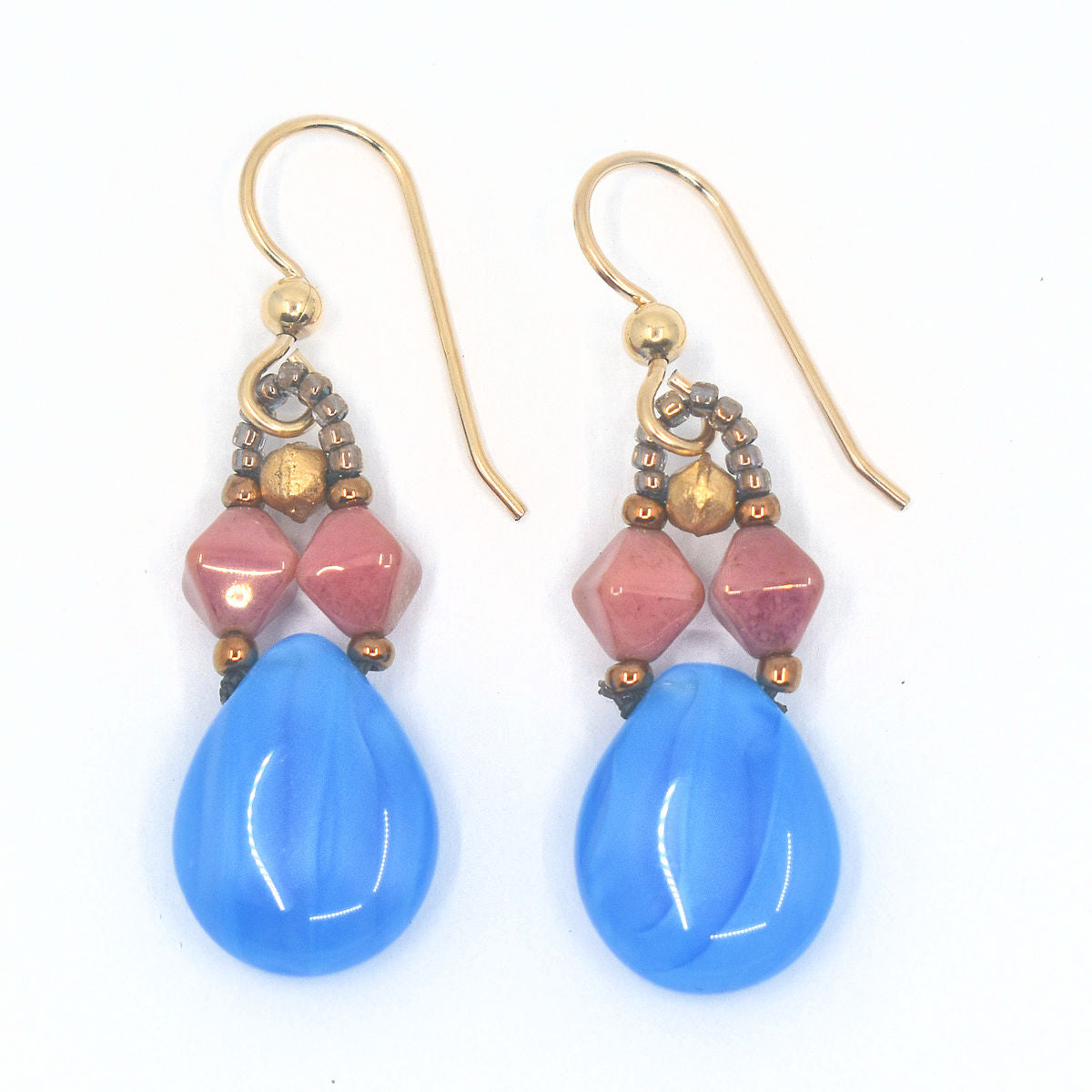 A pair of pink and blue earrings laying on a white background. The earrings are formed from large clear/blue striped glass suspended from light blue/clear swirl teardrops suspended from two parallel dusty pink double pyramids.