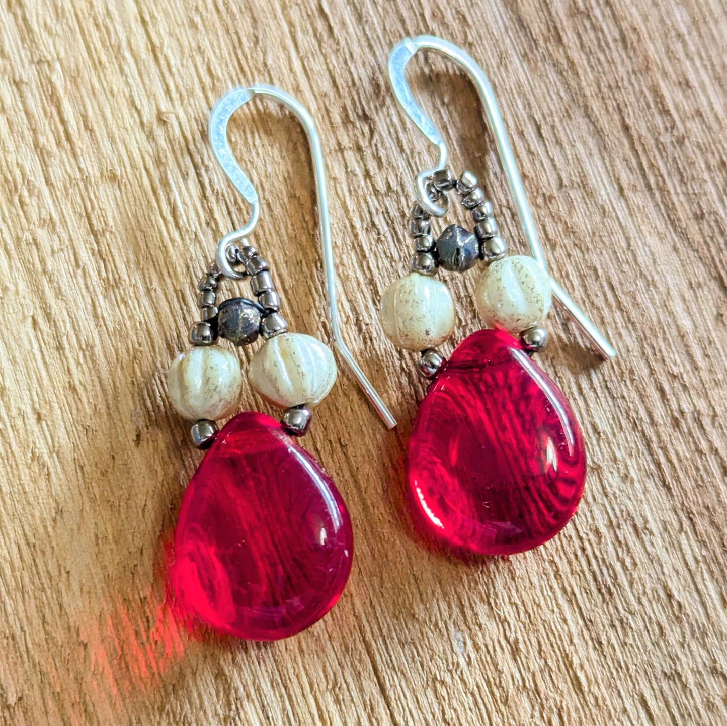 Pair of red teardrop earrings with white beads on a wooden surface