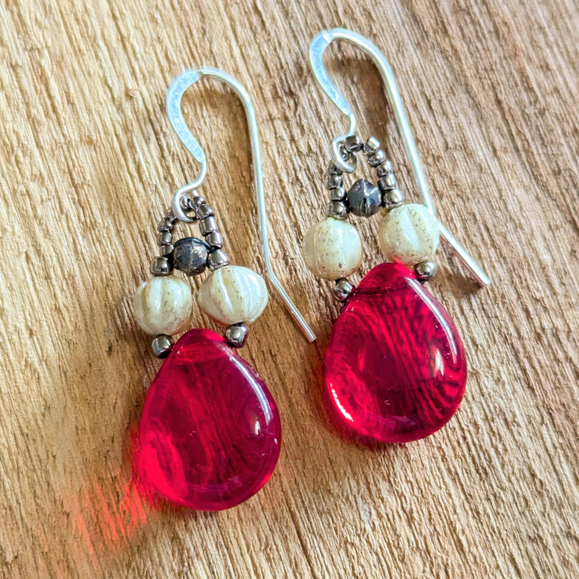 Pair of red teardrop earrings with white beads on a wooden surface