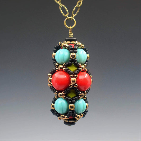 A turquoise and red pendant on brass chain hangs in front of a gray backrgound. The pendant has a central row of large red beads with a row of turquoise beads on either side. A netting of black and gold seed beads outlines all of the red and turquiose beads. 