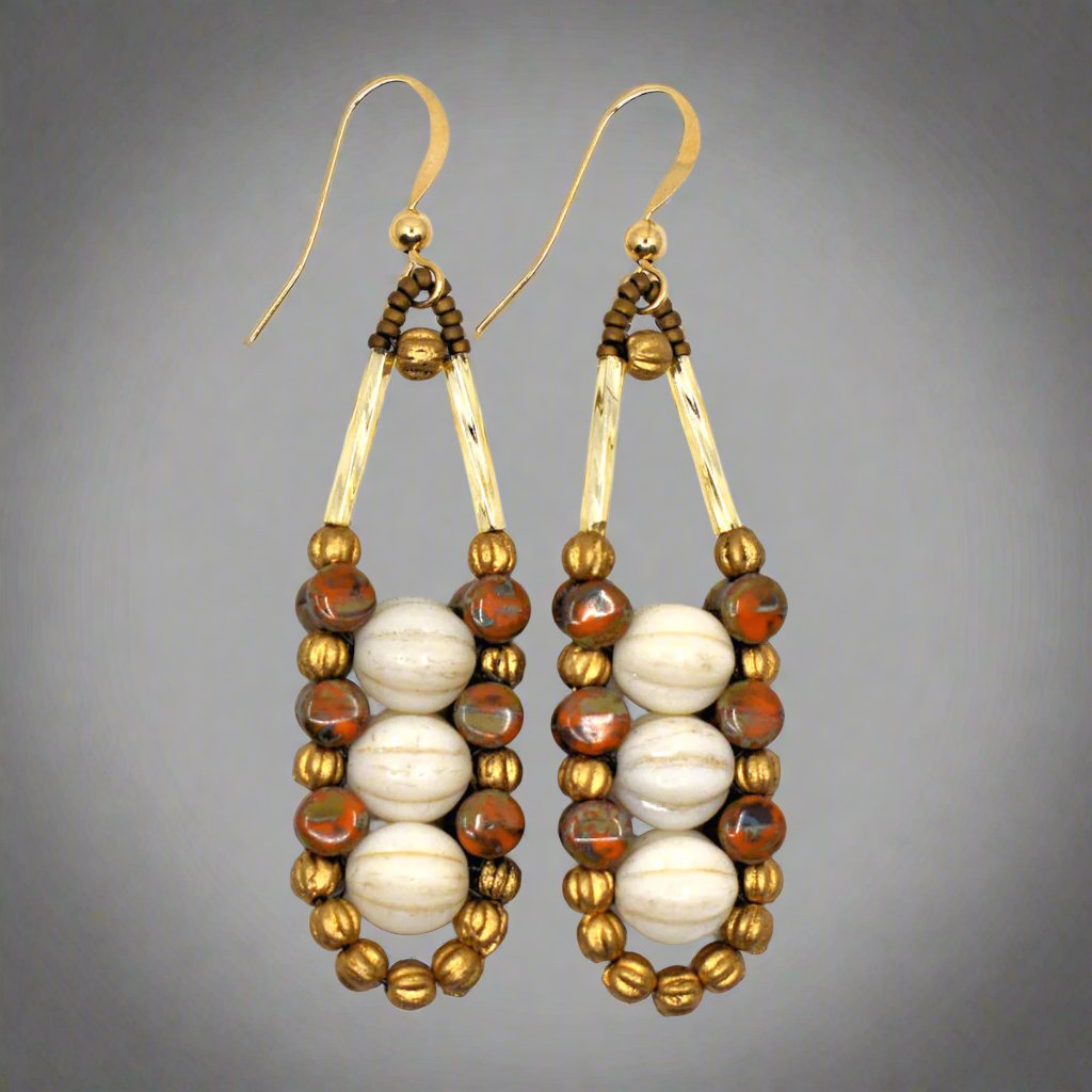 Cream, rust and gold accented earrings with gold ear wires on a white background. These earrings have three ridged cream rounds stacked vertically, held in place by an outline of speckled rusty orange and gold beads. 