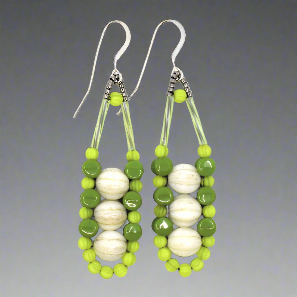 Cream and green earrings with silver accents and ear wires on a white background. These earrings have three cream rounds stacked vertically like peas and held in place by an outline of bright chartreuse and darker avocado green beads. 