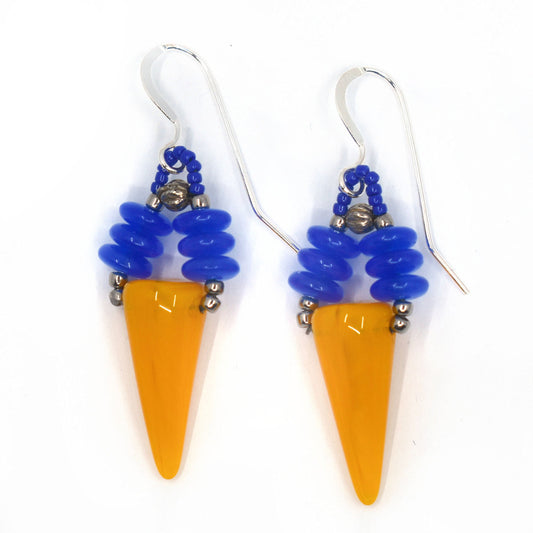 A pair of brightly colored earrings laying on a white background. The earrings have an upturned warm yellow cone suspended from two parallel stacks of blue discs.