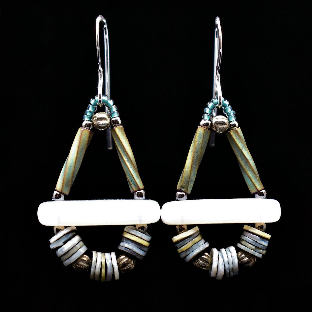 Silver, white and ocean colored earrings on a black background. The earrings have a triangle shape on top, with two iridescent green upright sides and a white bar at the base. Below the bar is an arc formed by three sections of blue-gray shell discs alternating with round silver beads.