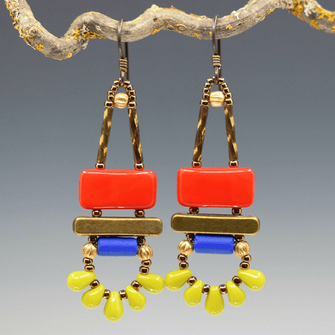 Red, blue, and lime green earrings with gold accents and dark ear wires hang from a lichen covered twig. The earrings have a red rectangle on top of a gold bar. Below the bar is a bright blue tube, and at the bottom is a swag of five small lime green drops separated by gold seed beads.