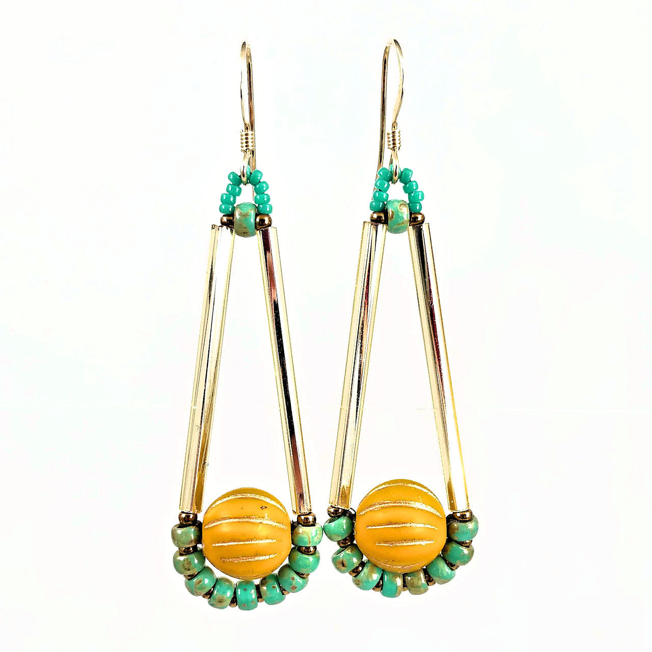 Long gold, turquoise and mustard earrings in an elongated teardrop shape against a white background. The earrings have gold ear wires. The upper part of the earring is formed by two shiny gold tubes, At the bottom is a round mustard yellow bead with gold lines on it. Around the bottom of the large bead is an arc of turquoise beads alternating with gold seed beads.