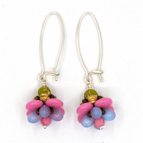 A pair of silver earrings with pastel pink and purple flower drops on a white background. The earrings have long silver oval wires that latch and the dangling parts are beaded flowers with pink outer petals and pale purplish blue inner petals.