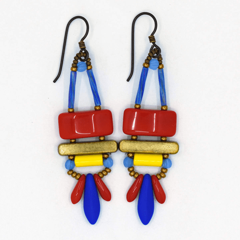Red, blue, and yellow earrings with dark ear wires and gold accents on a white background. These earrings have warm red rectangles on top of  gold tone bars. Below, a bright yellow tube sits above a swag of red and matte blue daggers.