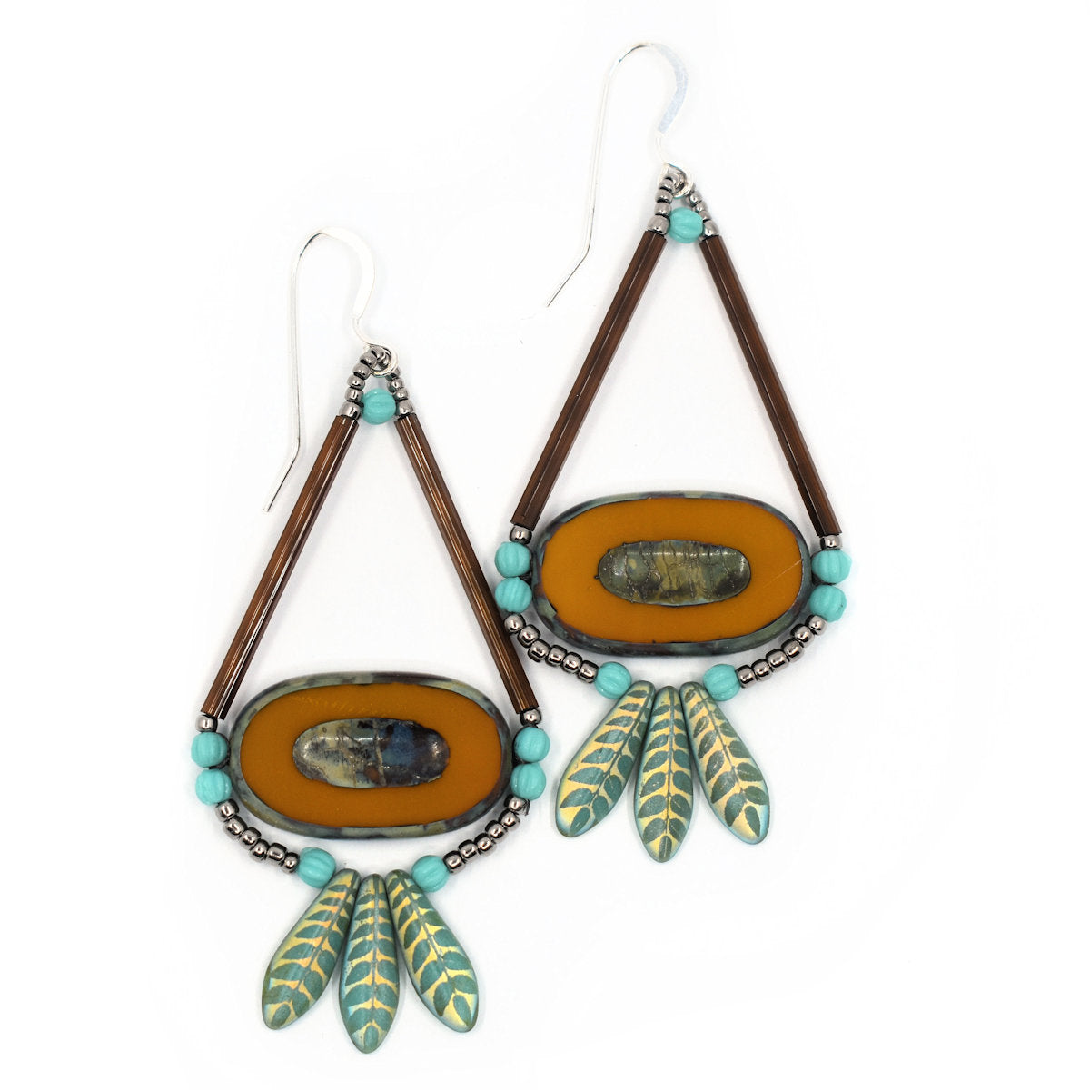 Orange and turquoise earrings shaped liked wide teardrops lay on a white background. The earrings have large orange oval beads that have a smaller speckled oval embossed into them. The ovals are suspended from two long brown tube beads that form a triangle. At the bottom of the ovals is a swag of small round turquoise beads, silver seed beads, and a fan of three gold-green dagger shaped beads that have a leaf pattern on them. The earrings have silver ear wires.