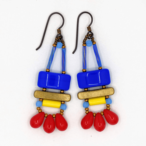 Blue, red, and yellow earrings with gold accents and dark ear wires on a white background. These earrings have a blue rectangle stacked on top of a gold bar. Below the bar is a yellow tube with light blue rounds on either side. On the bottom are three large red drops separated by gold seed beads.