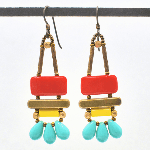 Red, yellow and turquoise earrings with gold accents and dark ear wires hang from a black bar against a white background. These earrings have red rectangles stacked on top of gold bars. Below the bars are bright yellow tubes. At the bottom are three large turquoise teardrops separated by gold seed beads.