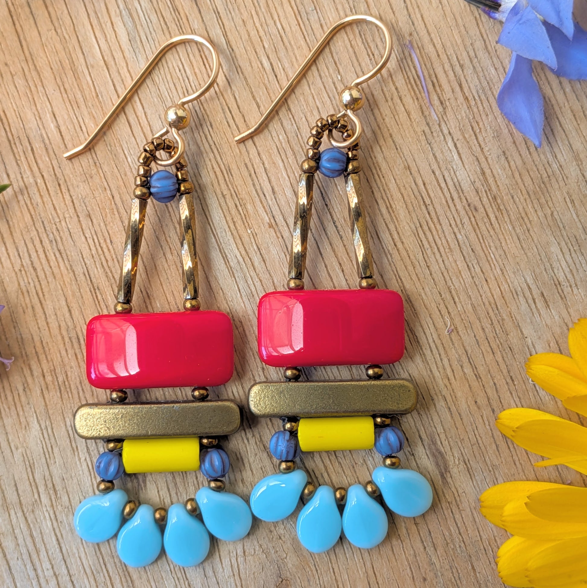 Green earrings on a wood background. Earrings with a white-striped, green rectangle on top of a gold bar, mint tube bar and a swag of four mottled turquoise petals.