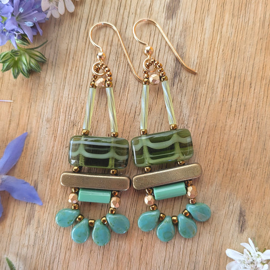 Green earrings on a wood background. Earrings with a white-striped, green rectangle on top of a gold bar, mint tube bar and a swag of four mottled turquoise petals.