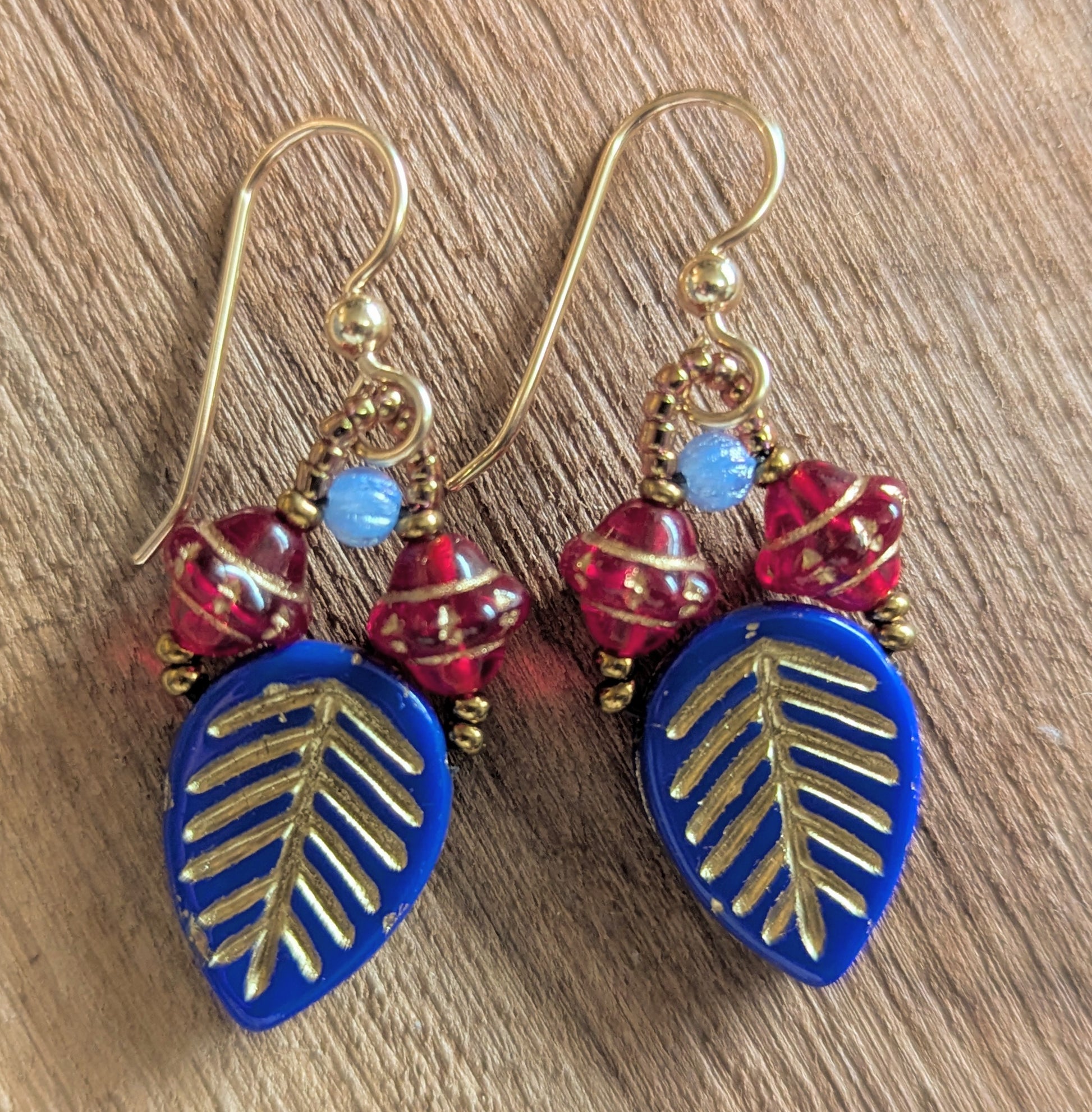 Pair of earrings with blue leaf-shaped drops and red beads on a wooden surface