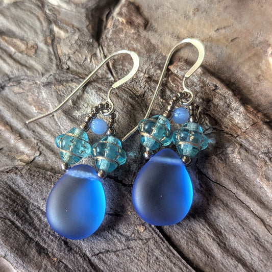Blue teardrop earrings with aqua beads on a stone surface