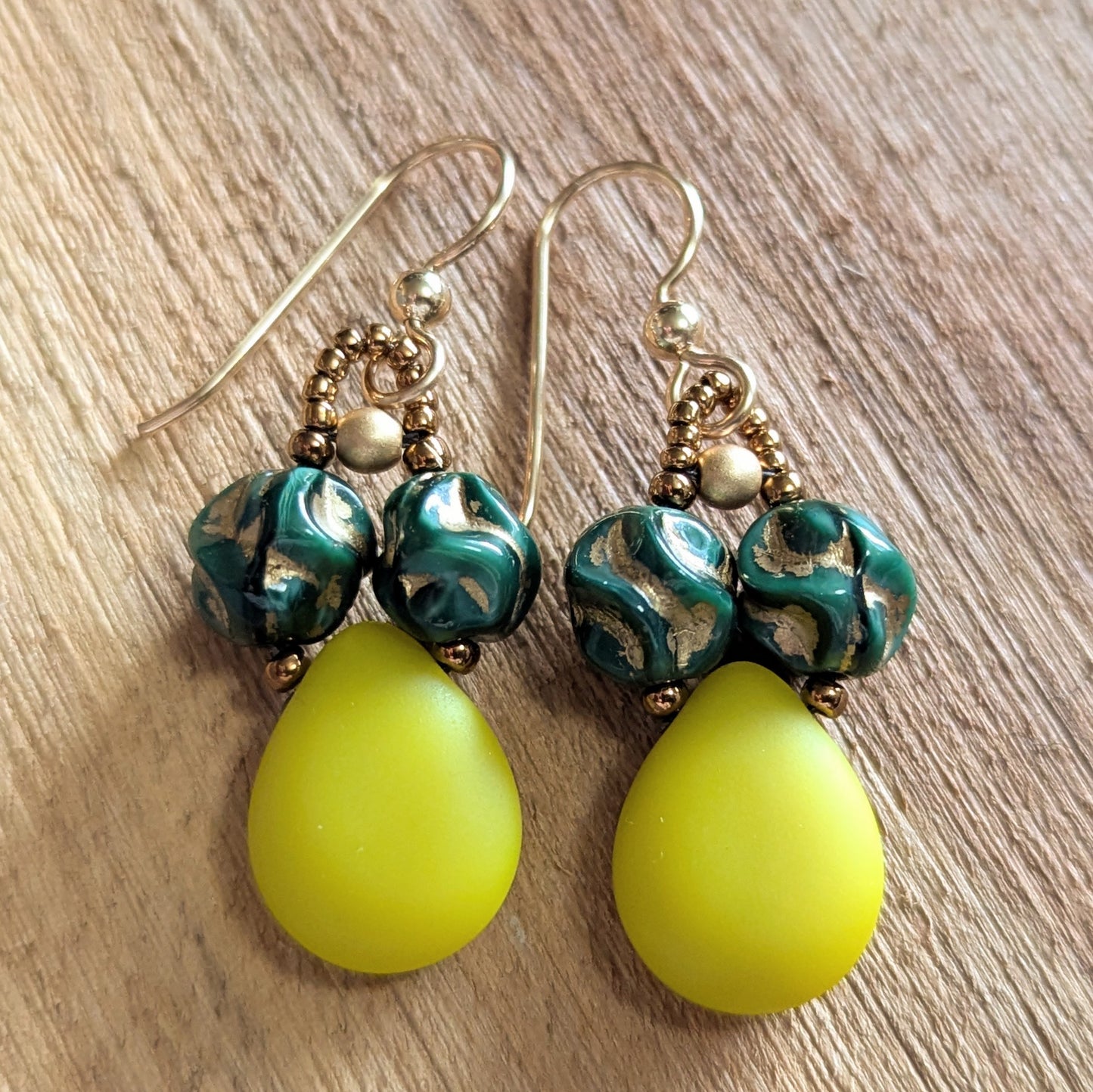 Pair of teardrop earrings with green and gold beads on a wooden surface
