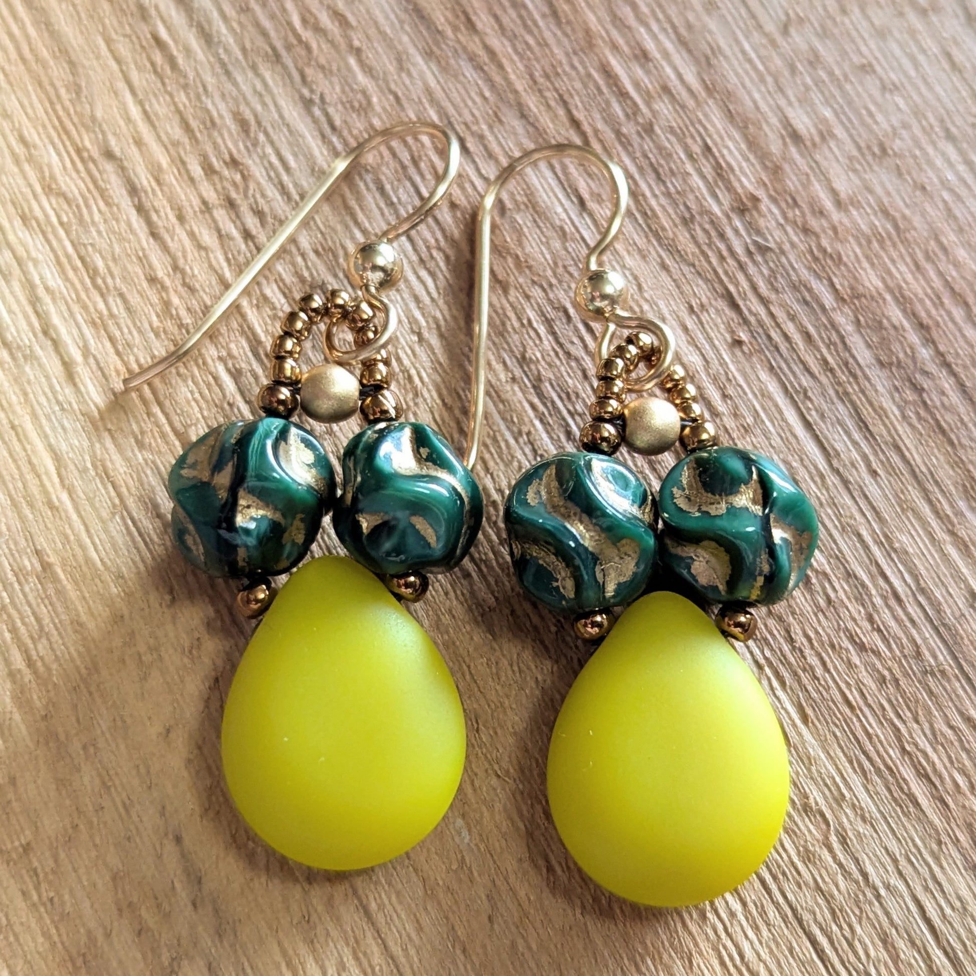 Pair of teardrop earrings with green and gold beads on a wooden surface