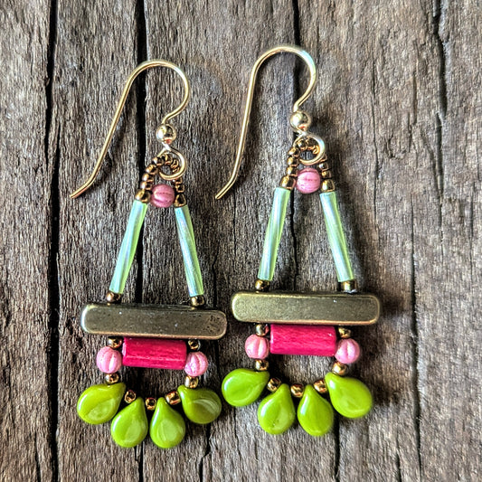 Colorful beaded earrings with gold, pink and green components on a wooden surface