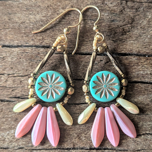 Earrings with turquoise center, gold accents, and pink and green fringe on a wooden surface