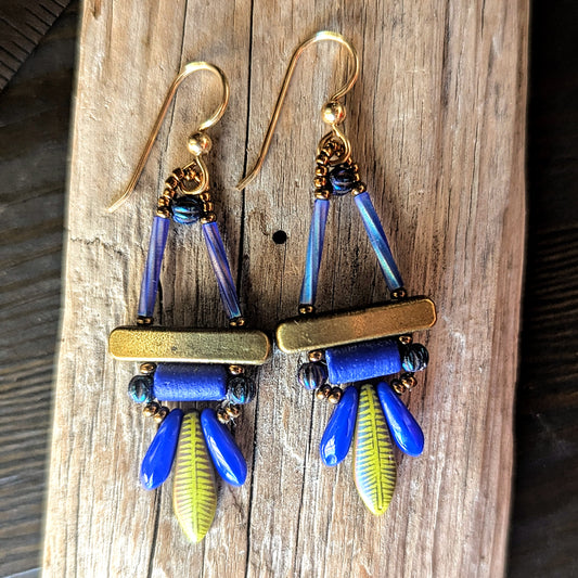 A pair of colorful earrings with gold, blue and olive green components on a wooden surface