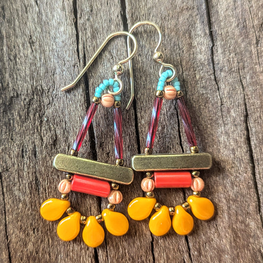 Colorful beaded earrings  with shades of orange, gold, and turquoise on a wooden surface.
