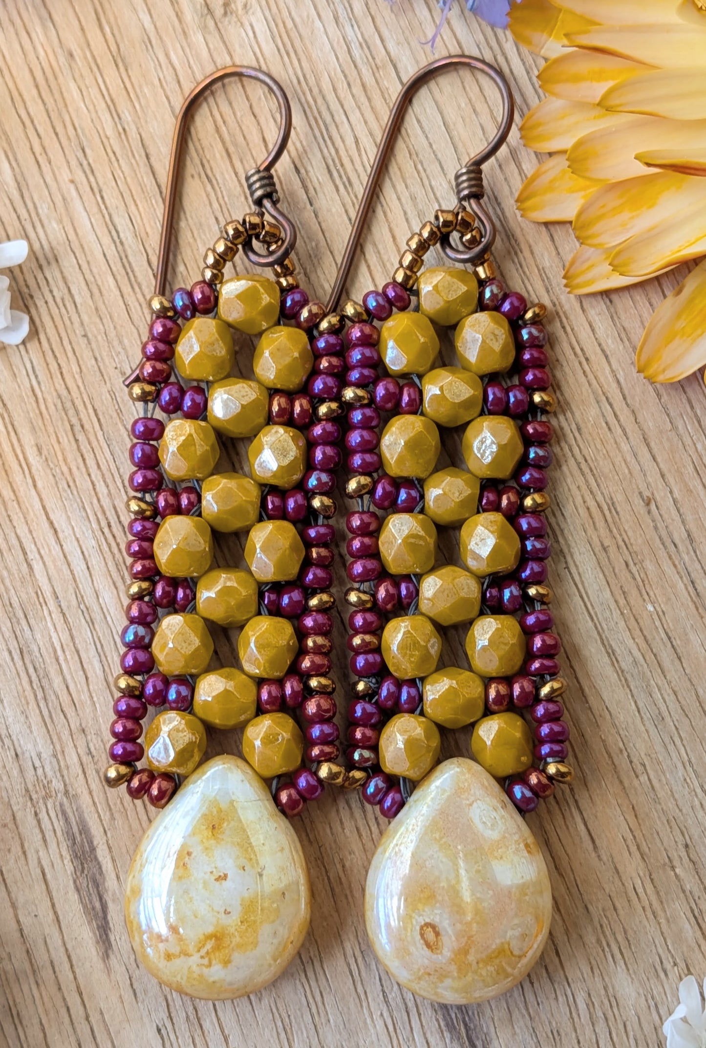 Yellow and purple beaded earrings with speckled cream teardrops at the bottom resting on a wood background.