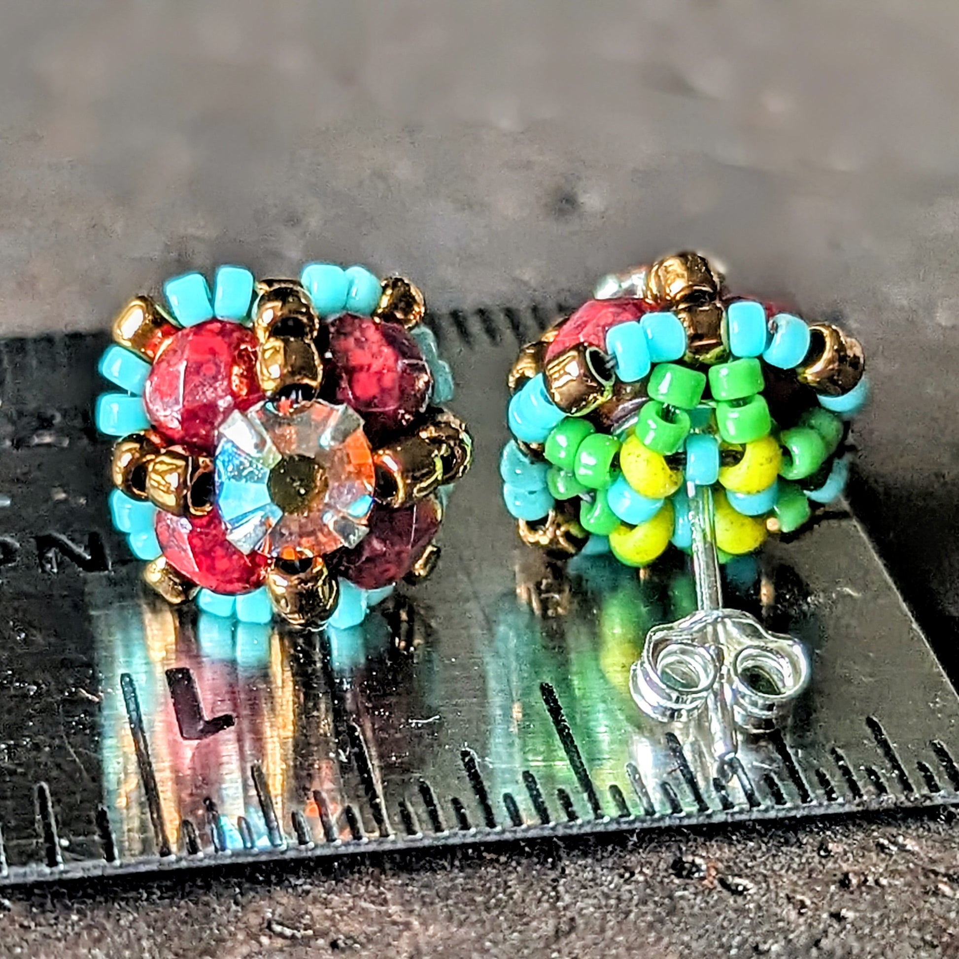 A pair of burgundy and turquoise stud earrings shown front and back on a ruler for scale. 