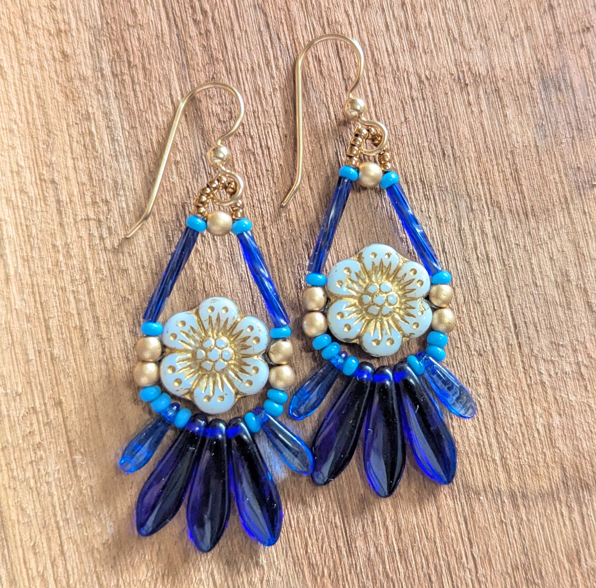 Beaded earrings with a white flower surrounded by blue and gold beads on a wooden surface