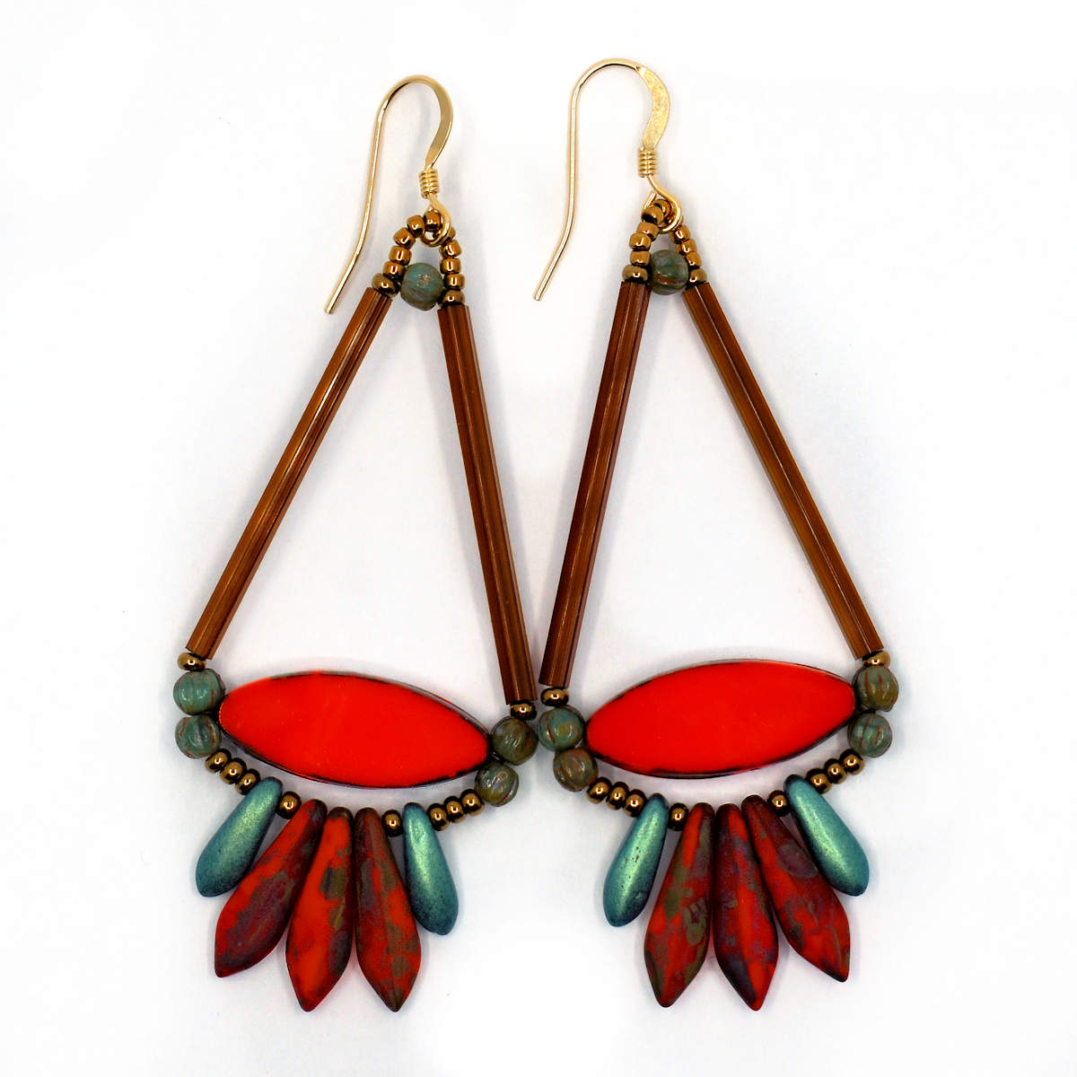 Long earrings shaped like a triangle with a curved fringe bottom lay on a white background. The earrings have two long brown tubes that form the top of the triangle shape and a narrow, pointy ended coral red oval at the bottom. Below the oval is a swag of coral red daggers with black speckles sandwiched between two smaller metallic green daggers. The earrings have gold ear wires and gold seed bead accents.